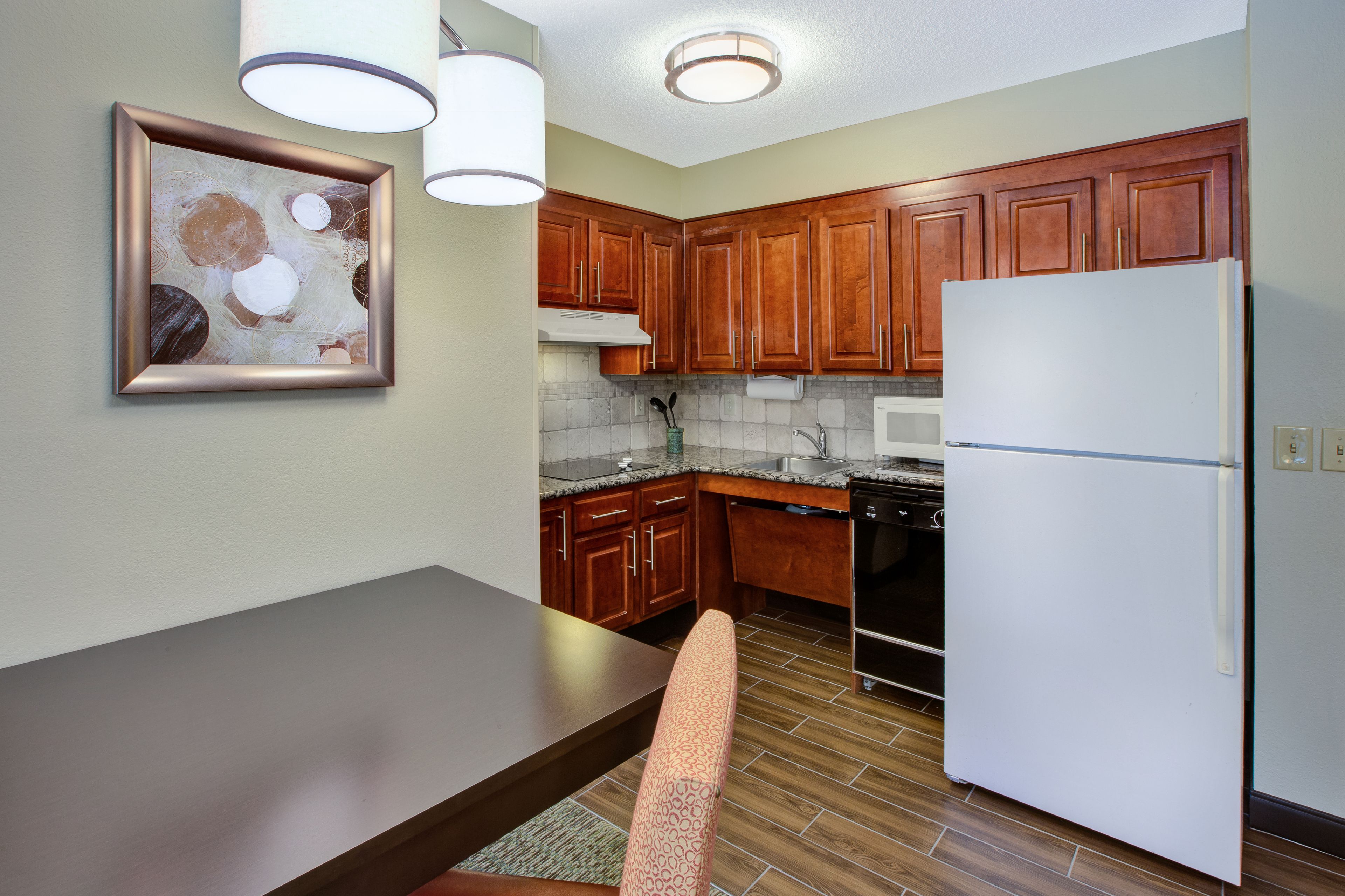 A kitchen with wooden cabinets, a white refrigerator, a microwave, and a dining table with a chair.