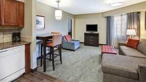 Een compacte hotelkamer met een kitchenette, een eethoek, een zithoek met een bank en fauteuil, een flatscreen-tv en een raam met gordijnen.