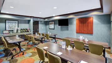 A conference room with a long table, multiple chairs, a coffee station, and a television on the wall.