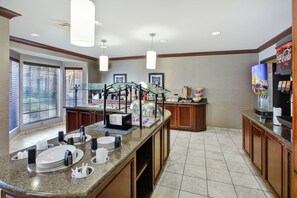 A hotel breakfast area with a self-serve station, beverage dispensers, and a Coca-Cola refrigerator.