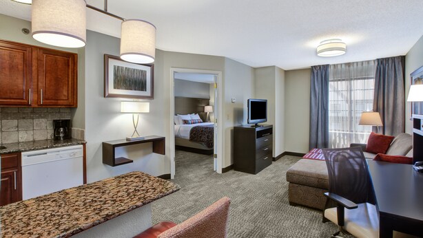 Een hotelkamer met een kitchenette, een bed, een bureau, een stoel en een televisie.