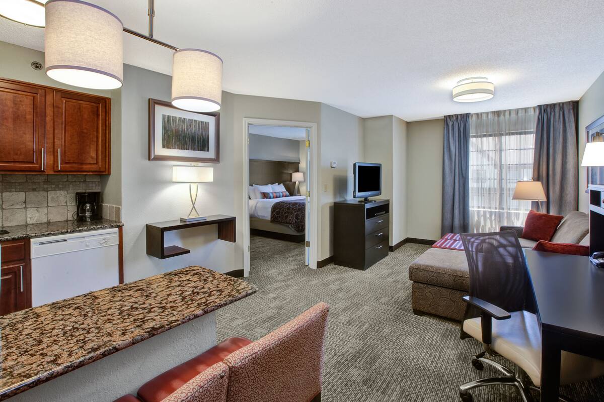 Une chambre d’hôtel équipée d’une kitchenette, d’un lit, d’un bureau, d’une chaise et d’un téléviseur.