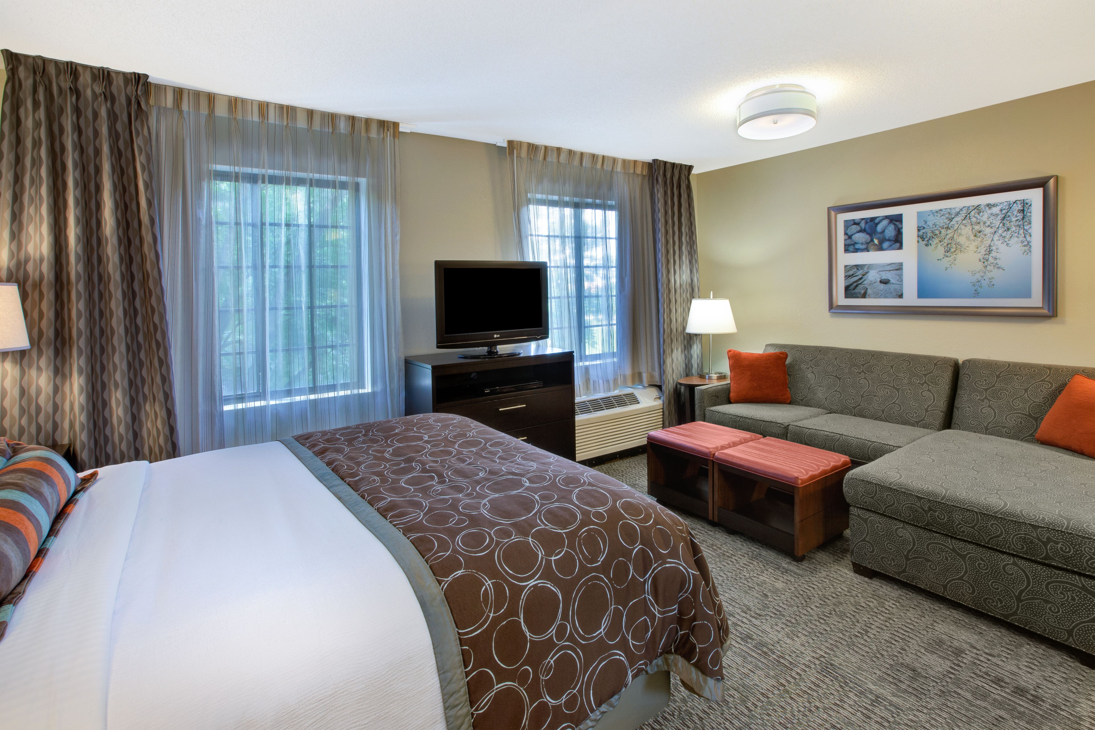 A hotel room with a bed, a sofa, a TV, and a desk with a lamp.