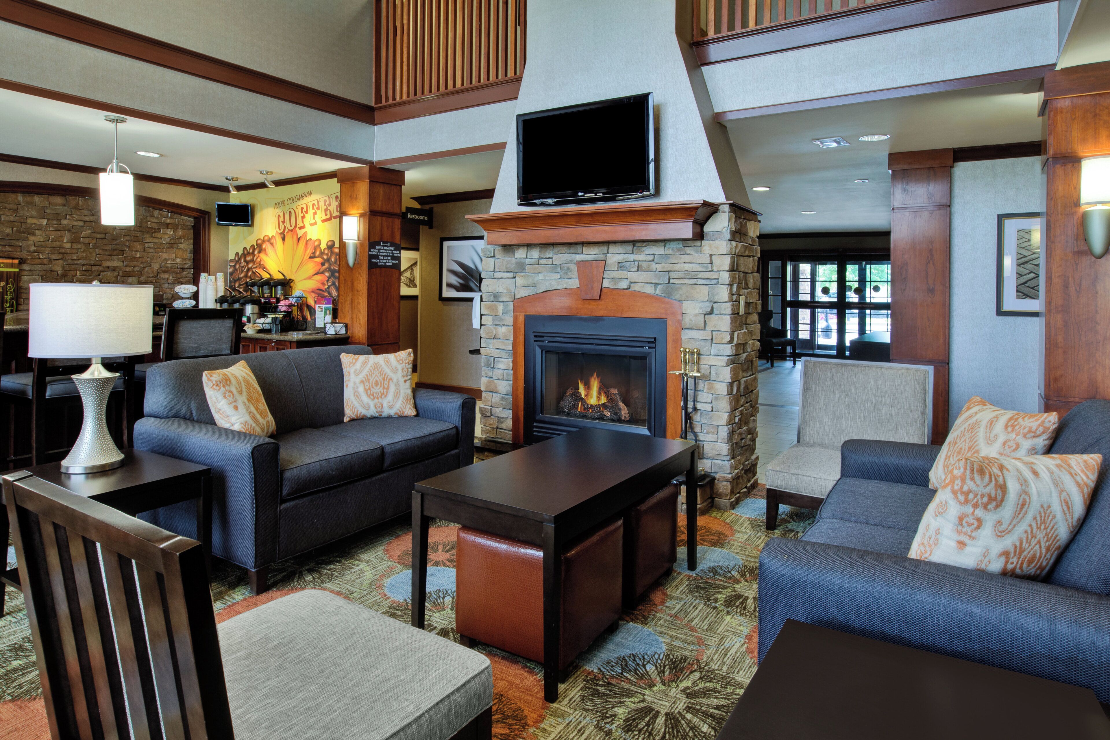 A hotel lobby with a fireplace, sofas, a coffee station, and a television.