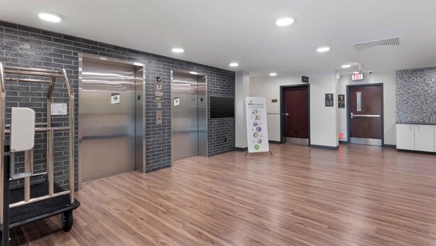 A modern elevator area with a metal cart, two elevators, a sign, and a patterned wall. - Extended Stay America Premier Suites Miami Downtown Brickell (Miami)