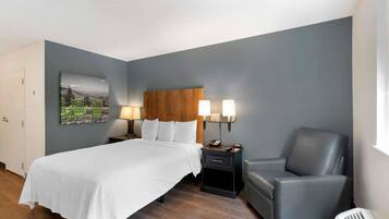 Habitación de hotel con cama, mesita de noche con lámparas, una silla y un estante en la pared.