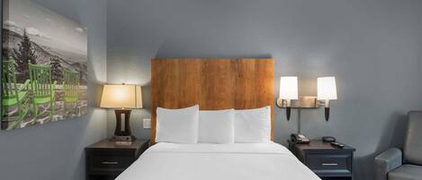 A hotel room with a bed, two bedside tables, a chair, a lamp, and a wall-mounted light fixture.