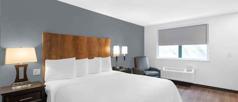 Ein Hotelzimmer mit einem großen Bett, einem Nachttisch mit Lampe, einem Sessel und einem Fenster mit Blick.