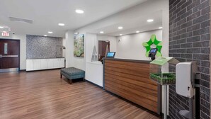 A reception area with a wooden reception desk, a green wall-mounted digital screen, a trash bin, and a reception counter. - Extended Stay America Premier Suites Miami Downtown Brickell (Miami)