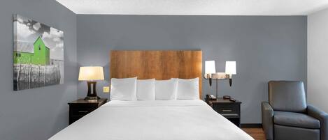 Une chambre d’hôtel avec un grand lit, deux tables de chevet avec des lampes, une chaise et des œuvres d’art accrochées au mur.