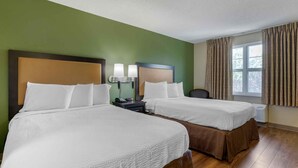 A hotel room with two beds, a nightstand with a phone, and a window with curtains.