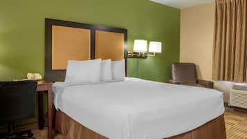 Quarto de hotel com uma cama grande, uma escrivaninha com telefone, uma cadeira e uma luminária na parede.