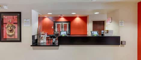Un espace d’accueil d’hôtel comprenant un comptoir de réception, une œuvre d’art encadrée et un mur d’accent rouge.