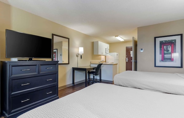 A hotel room with a bed, a desk, a television, a dresser, and a kitchenette.