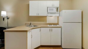 A compact kitchen with white cabinets, a microwave, a refrigerator, and a sink.