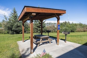 A wooden pavilion with a picnic table, a mailbox, and an American flag on a concrete base.