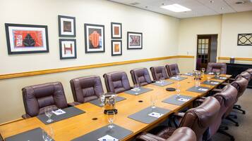 A conference room with a long table, brown leather chairs, framed artwork on the wall, and a door in the background.