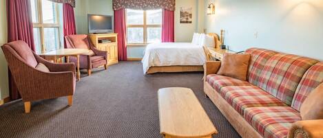 A hotel room with a bed, a sofa, a chair, a small table, and a TV.