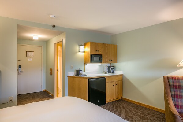 A hotel room with a bed, a kitchenette with a microwave, a sink, and a small refrigerator. - Sugarloaf Mountain Hotel (Kingfield)