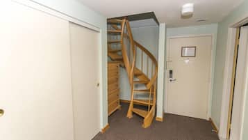 A hallway with a wooden spiral staircase, a door with a lock, and a carpeted floor.
