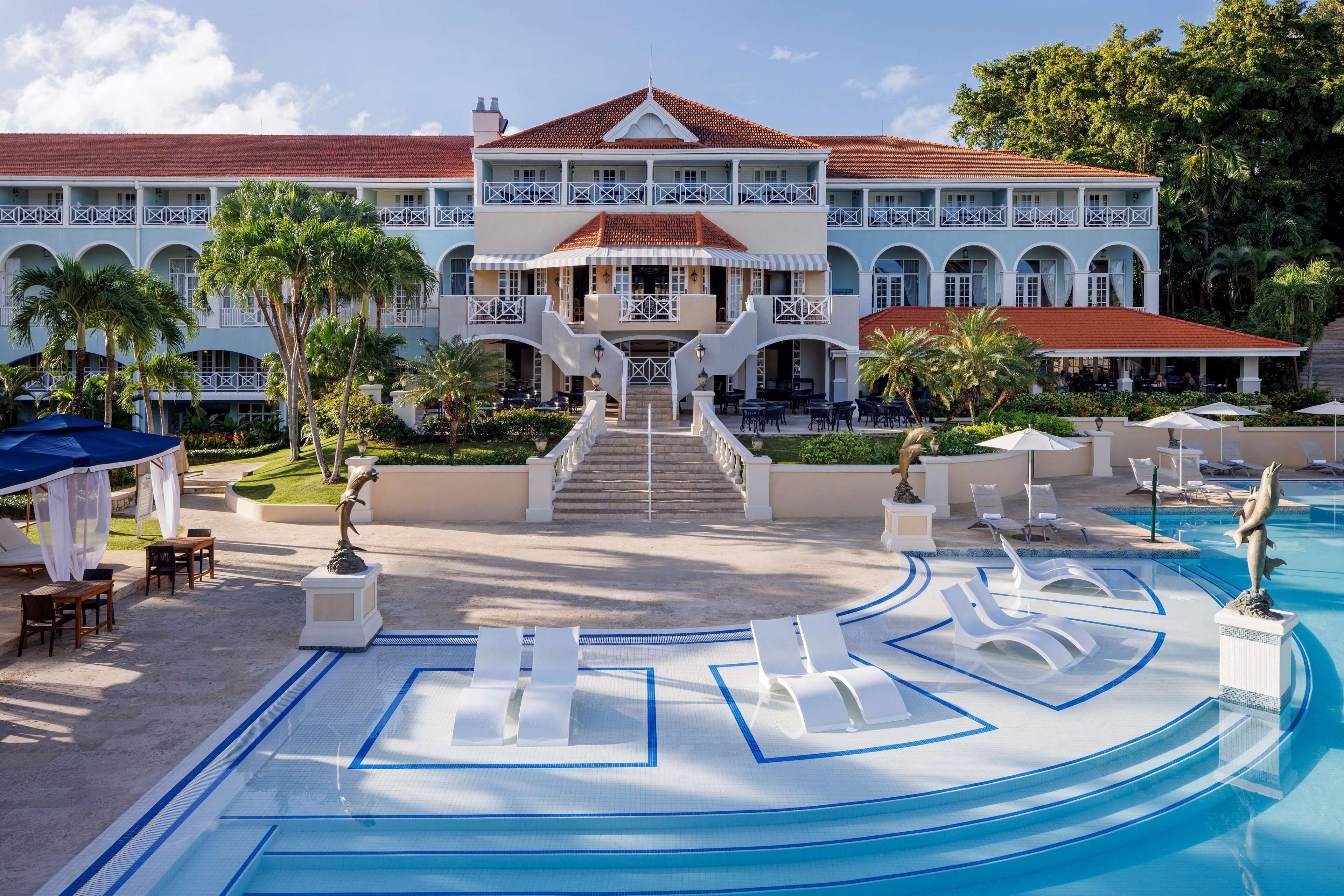 A resort with a large pool, outdoor seating, and a grand building with a red roof.