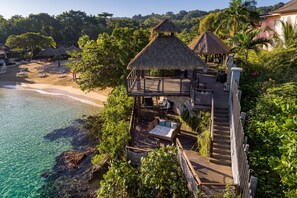 A beachside resort with thatched-roof structures, a wooden deck, and a clear view of the ocean.