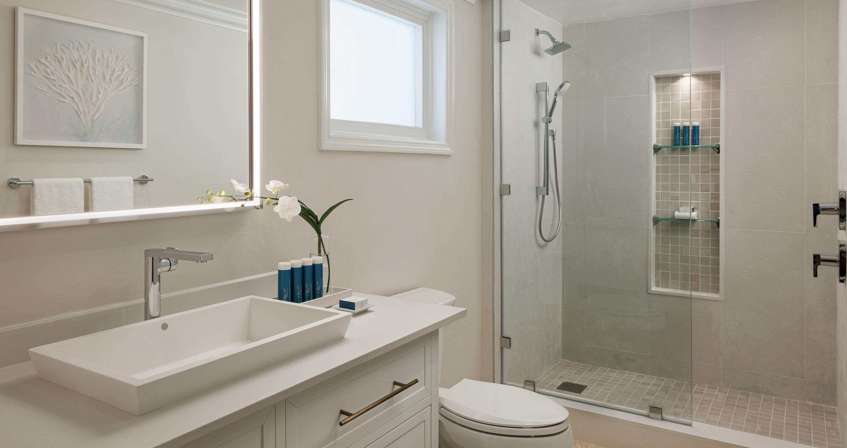 A modern bathroom with a large mirror, a white sink, a toilet, and a glass-enclosed shower.