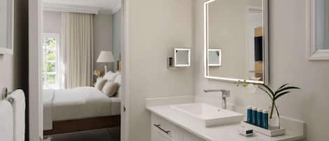 Una habitación de hotel con una cama grande, un tocador blanco con espejo y una pequeña planta en maceta.