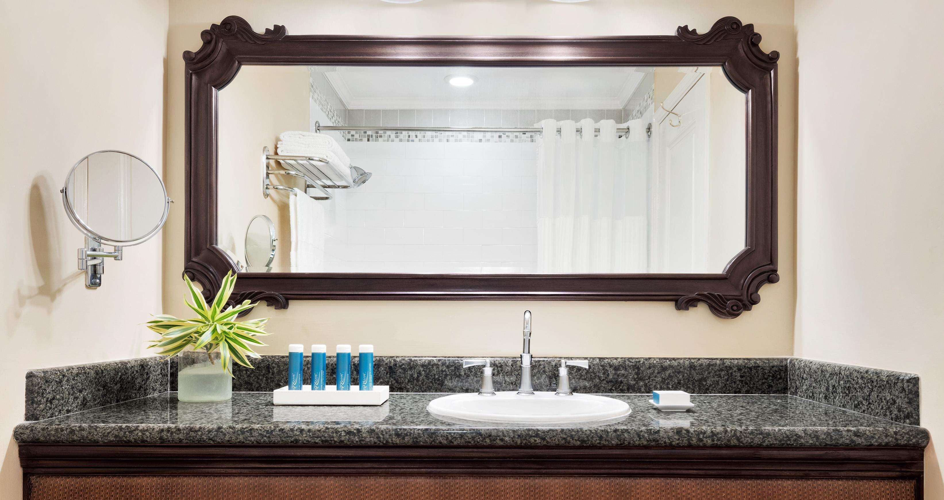 A bathroom with a granite countertop, a sink, a mirror, and a shower area.