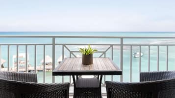 Ein Balkon mit Holztisch und Korbstühlen, mit Blick auf das türkisfarbene Meer und eine Hotelanlage.