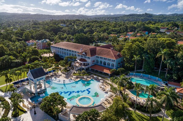 A resort with a large central pool, multiple guest buildings, and lush surrounding greenery.