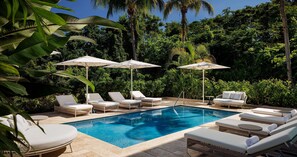 A pool area with lounge chairs and umbrellas, surrounded by lush greenery.