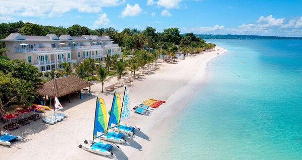 A beachfront hotel with multiple balconies, a beach with paddleboards, and a clear view of the ocean.