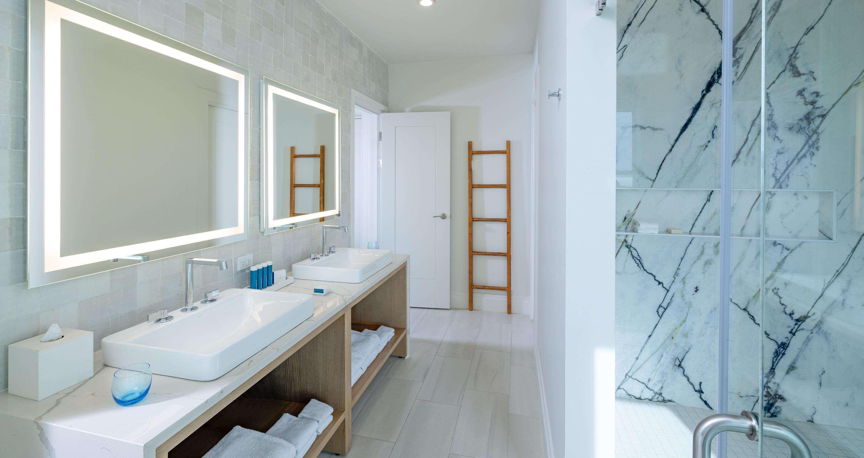 Une salle de bain moderne avec deux lavabos, un grand miroir et une douche aux carreaux de marbre.