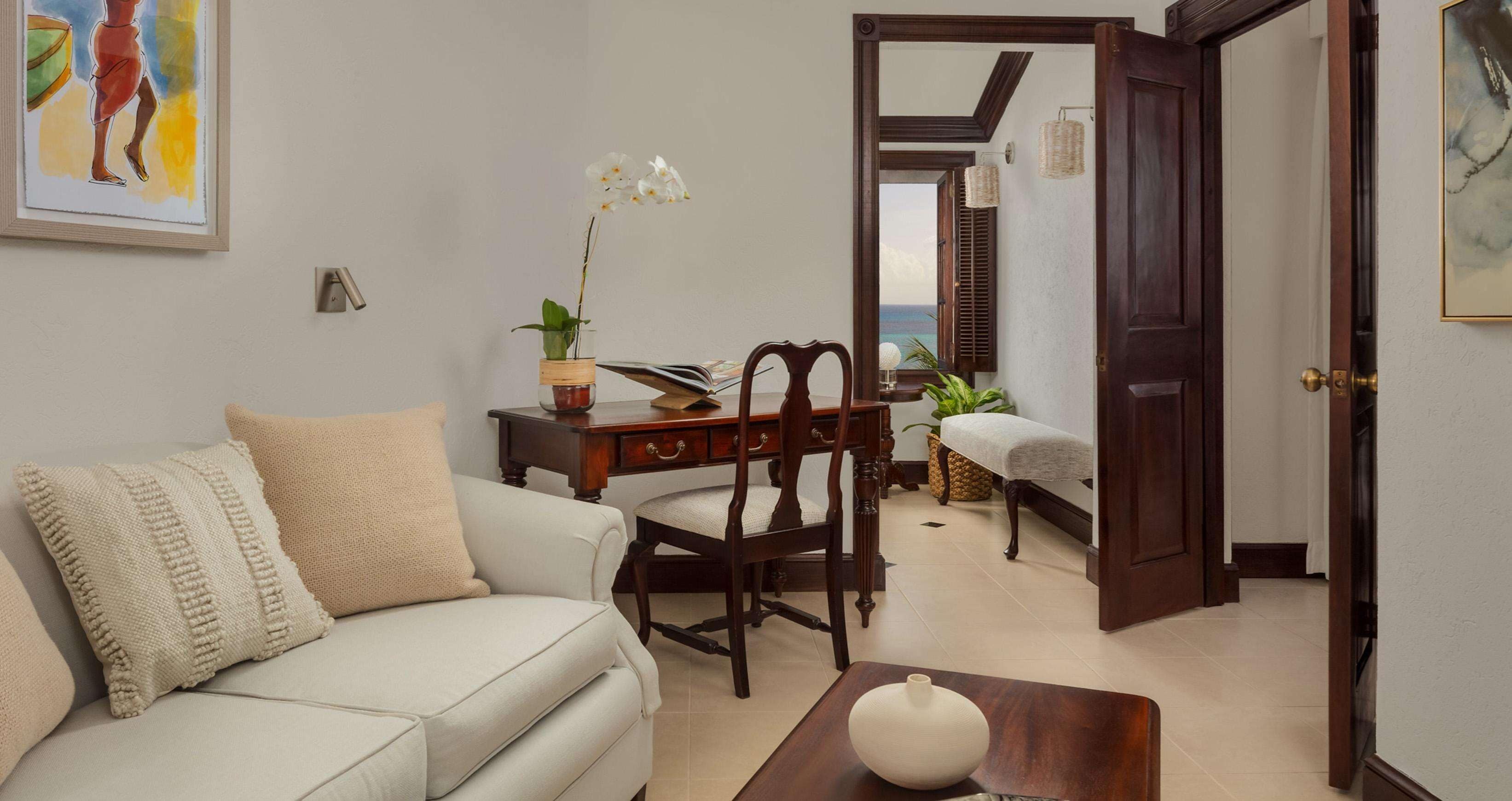 A living room with a sofa, a wooden table, and a chair. There is a door leading to another room.