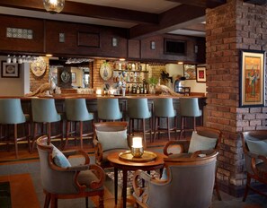 A bar area with multiple seating options, including bar stools and cushioned chairs, with a variety of bottles and glasses on the bar counter.