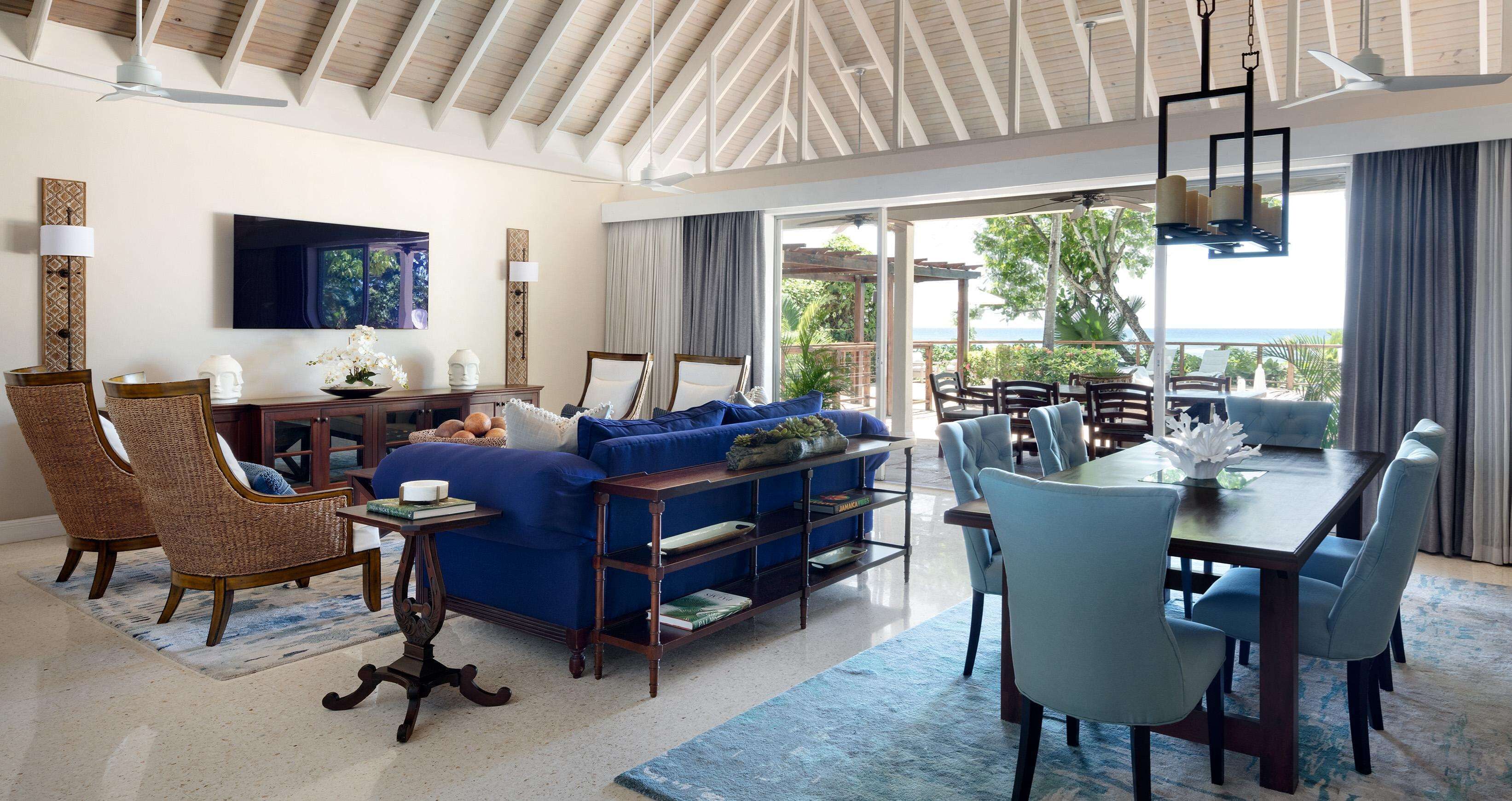 A spacious living area with a blue sofa, wicker chairs, a dining table, and a large TV.