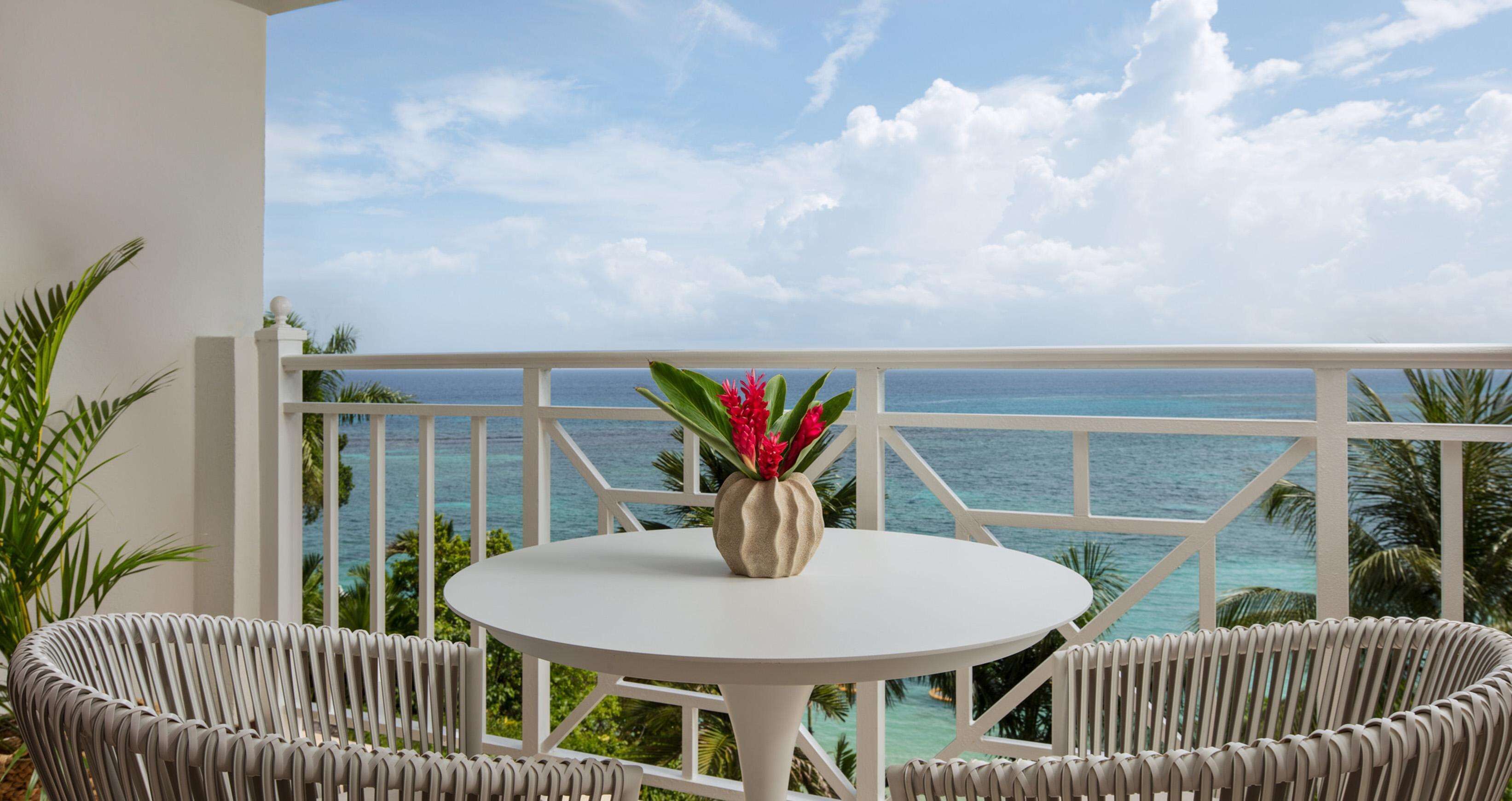 A balcony with a white railing, a round table, and two wicker chairs.