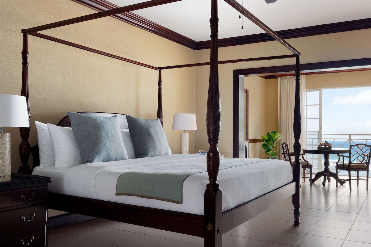 A four-poster bed with a view of the sea, a dining area with a table and chairs, and a balcony with a view.