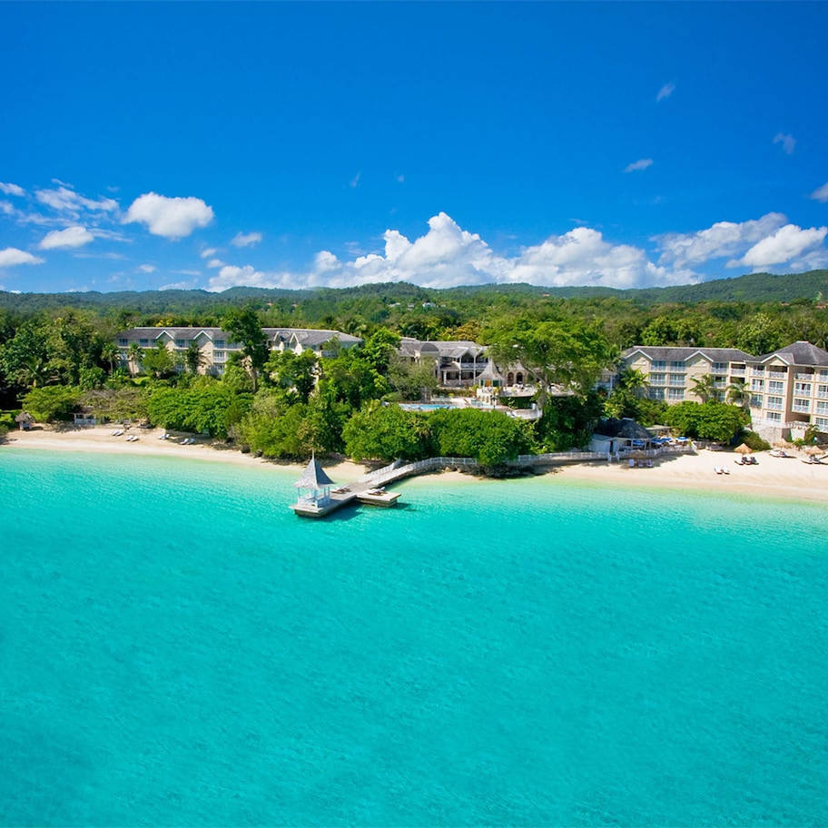 A resort with multiple buildings, a beach, and a clear blue sea.