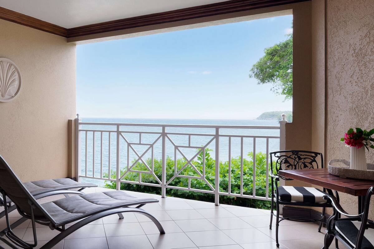 A balcony with a view of the sea, a round decorative wall piece, and a table with chairs.