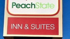 A sign for Peach State Inn & Suites with a logo featuring a peach and a person. - Peach State Inn & Suites (Hawkinsville)