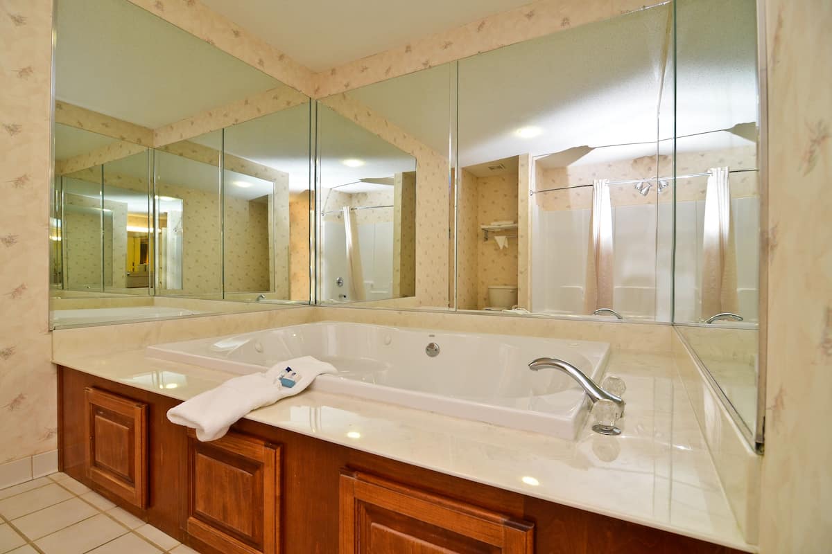 A bathroom with a large mirror, a bathtub, and a vanity with a towel.