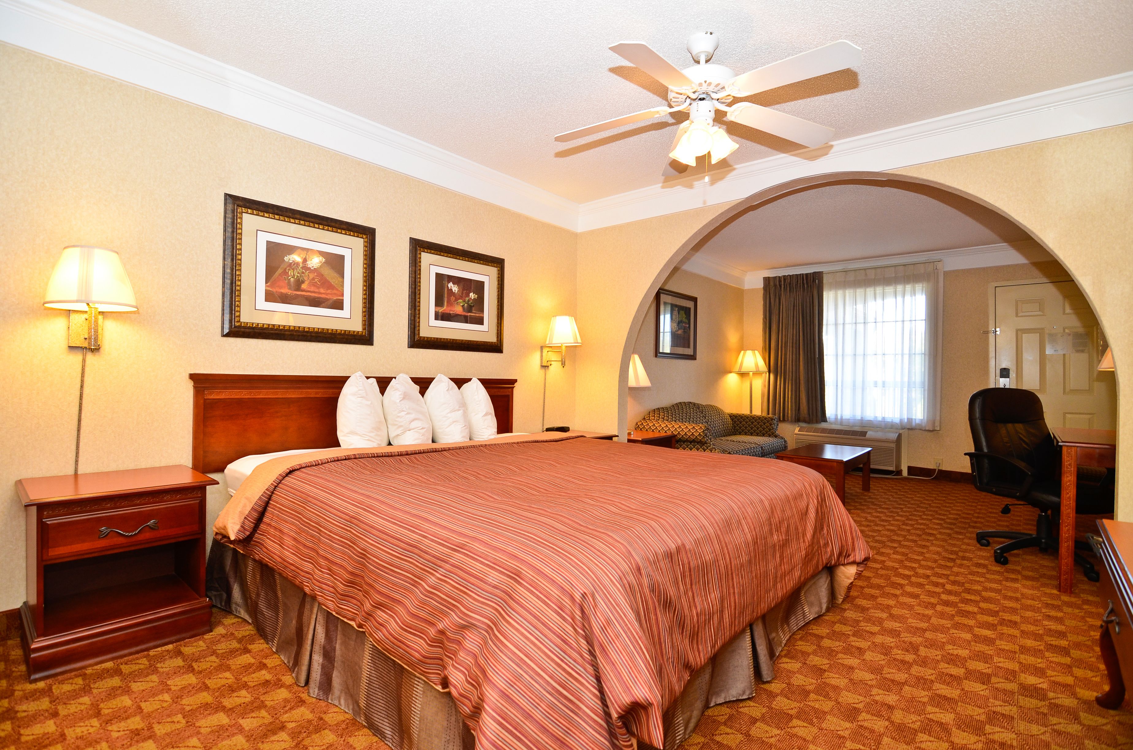 A hotel room with a large bed, two wall-mounted lamps, a ceiling fan, and an arched doorway leading to another room.