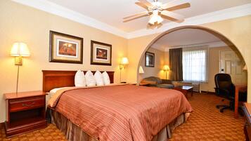 A hotel room with a large bed, two wall-mounted lamps, a ceiling fan, and an arched doorway leading to another room.
