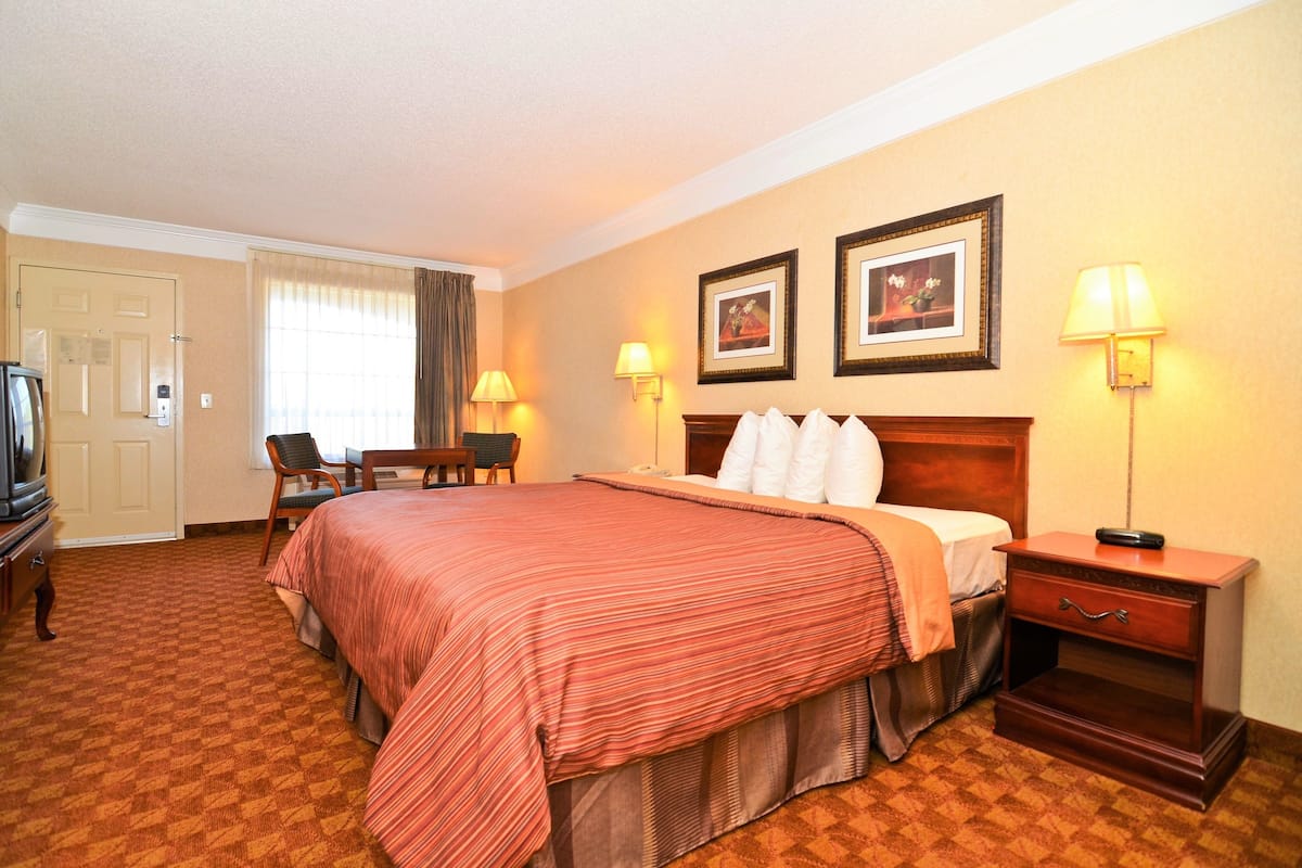 A hotel room with a large bed, a desk, two chairs, a television, and two wall-mounted lamps.