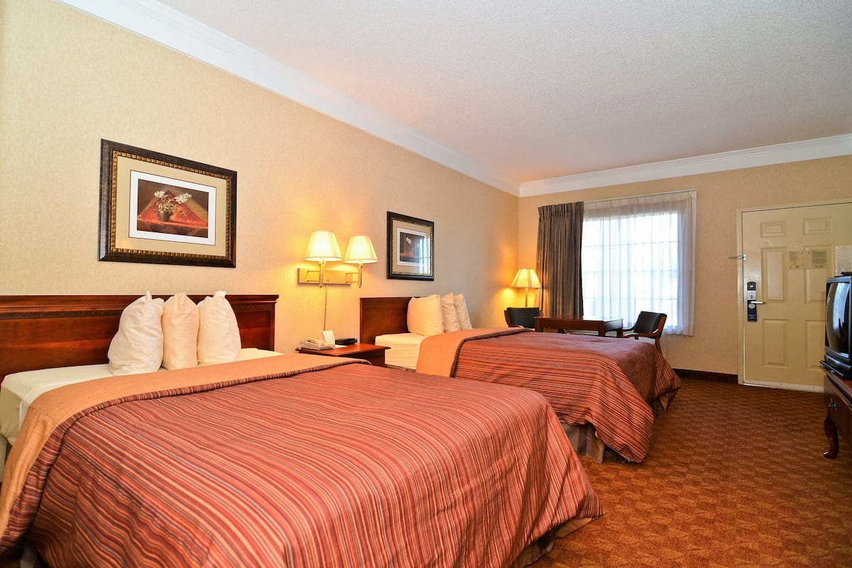 A hotel room with two beds, a TV, a desk, and a window with curtains.