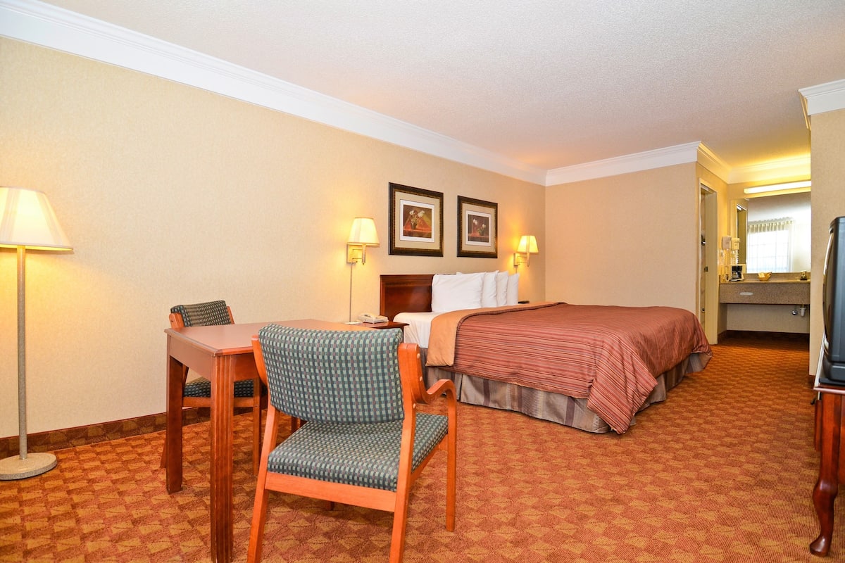 A hotel room with a bed, a desk with a chair, two wall-mounted lamps, and framed pictures on the wall.