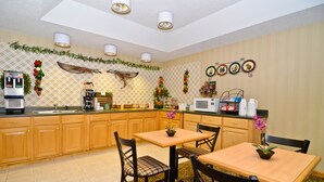 A kitchen with wooden cabinets, a coffee machine, a microwave, and a dining area with two chairs and a table. - Peach State Inn & Suites (Hawkinsville)