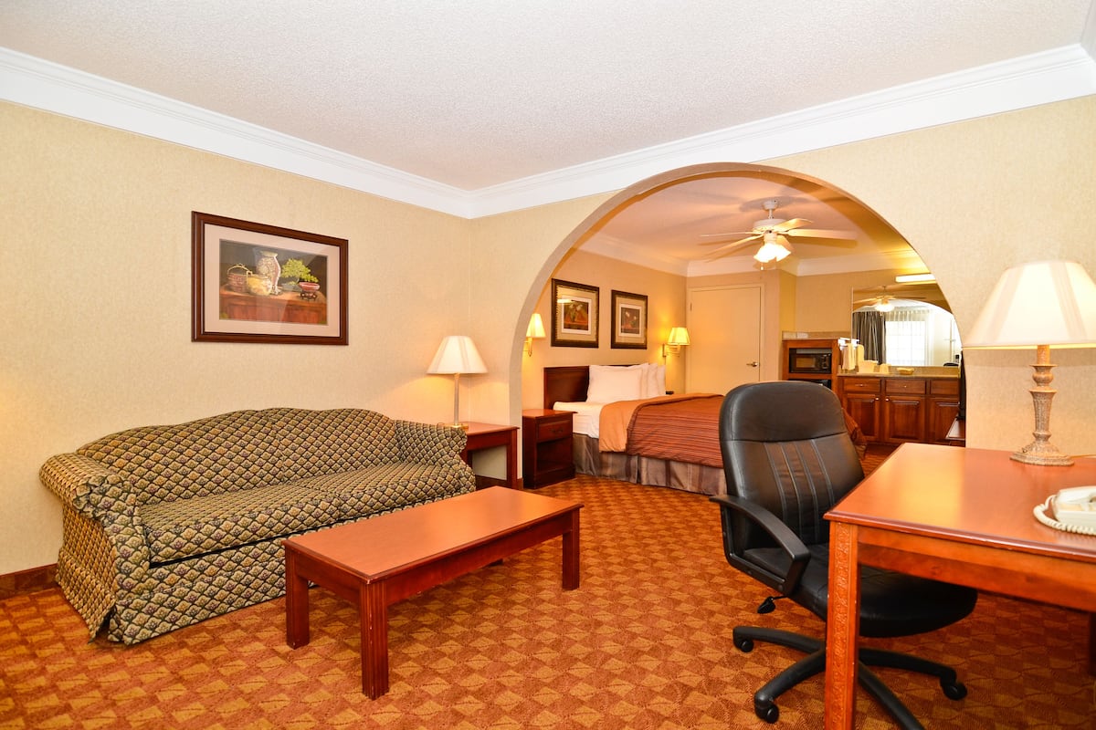 A hotel room with a sofa, a desk, a chair, a bed, and a bathroom visible through an archway.